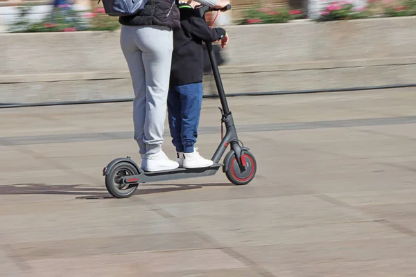 Mãe e filho montando scooter elétrico chute na praça da cidade — Fotografia de Stock