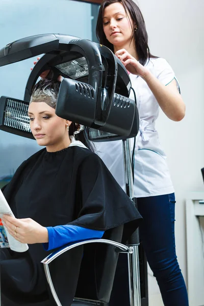 ヘアケア リラクゼーション ヘアスタイ リングのコンセプトです 乾燥機械の下で彼女の髪を取得黒マントに座っている女性 — ストック写真