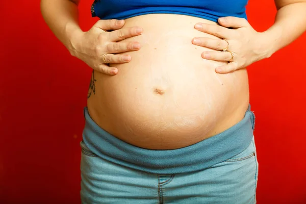赤ちゃん概念を待っています 大人の女性は 彼女の大きな妊婦腹を示します 赤の背景に屋内のショット — ストック写真