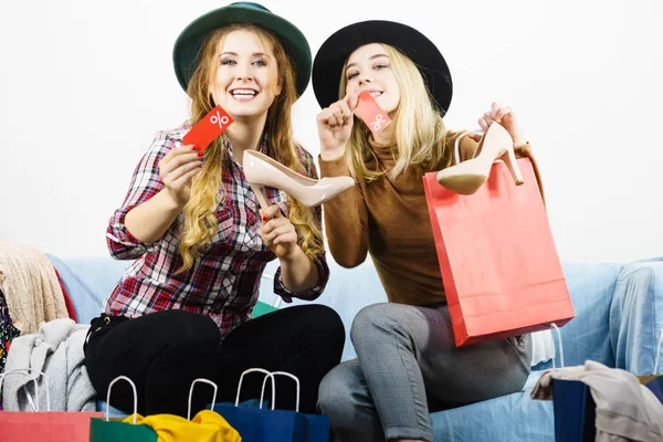 Female friends on shopping showing tag with sale percentage sign enjoying cheap clothing.