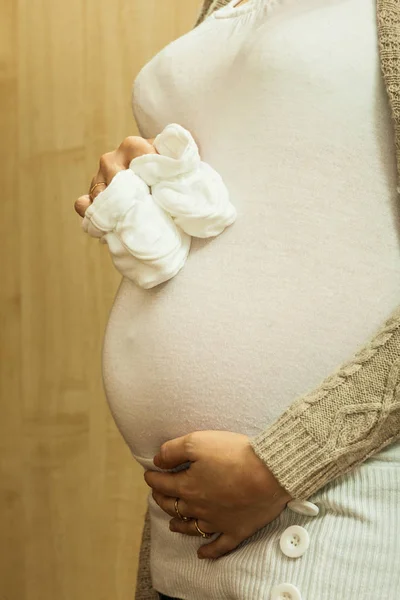 母性の概念 妊娠中の女性の白い赤ちゃん靴下を押し 彼女の腹に触れる — ストック写真