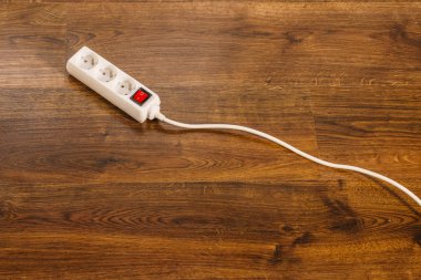 Electricity at home. White electric power strip or extension cord block for extending plug with red switch on off, on wooden floor. clipart