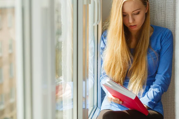 坐在窗台上的年轻女子阅读有趣的书 享受她的放松时间透过窗户看 — 图库照片