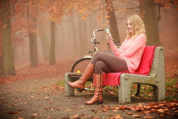 技術スマート フォン自然屋外サイクリングのコンセプト 音楽を聴いている女の子を笑っています ヘッドフォンを身に着けているバイク楽しんで音 の横のベンチに座って公園の若い女性 — ストック写真