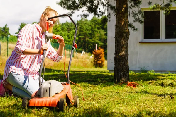 Gardening. Female person being mowing green lawn with lawnmower, in sunny day.