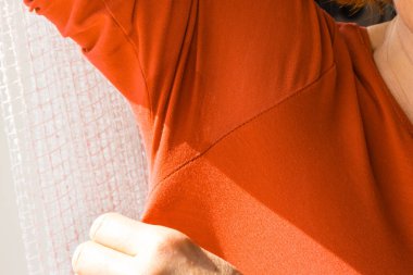 Woman having sweat stains on orange shirt with long sleeve. Diaphoresis problem concept. clipart