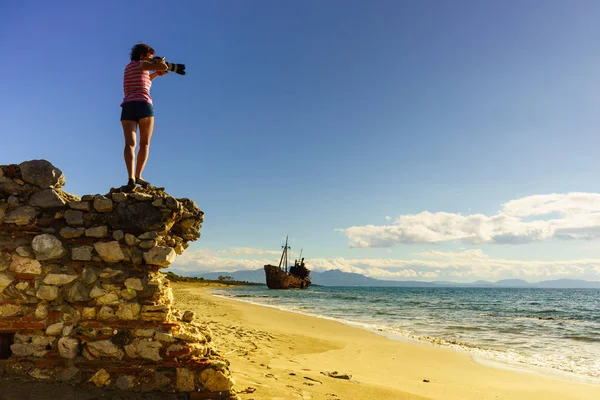 観光休暇や旅行 ビーチでの女性観光客のカメラで写真を撮る 背景に難破船 — ストック写真