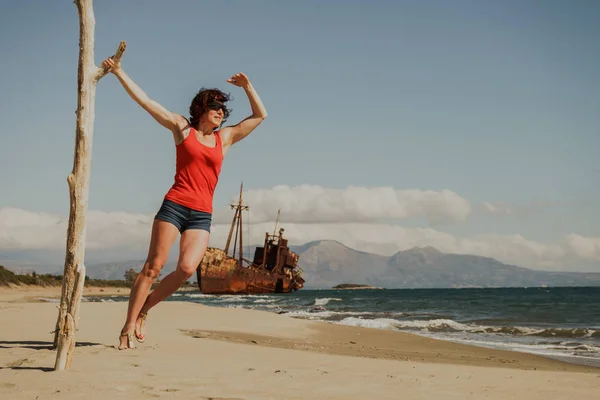旅行自由 海滩上成熟的女游客享受暑假 一艘废弃的旧船在后面失事的船 — 图库照片