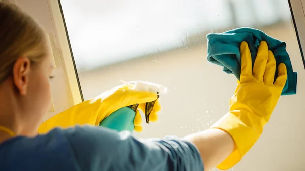 穿着黄色手套的年轻女子用蓝色抹布和喷雾洗涤剂清洗窗户 春季清洁 家务活概念 — 图库照片