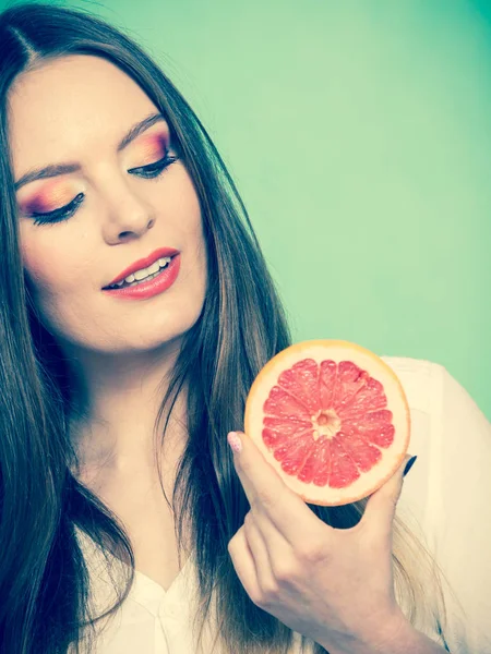 グレープフルーツ柑橘系の果物の半分を手に女性の魅力的な長い髪の女の子 健康的な食事 夏休みの休暇のコンセプト 緑のスタジオショット — ストック写真