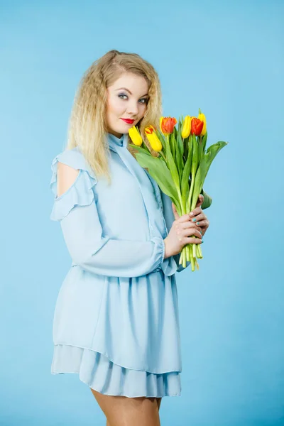 International women day, eight march. Beautiful portrait of pretty woman blonde hair with red yellow tulips, fashion make up, elegant dress. Mother day. On blue