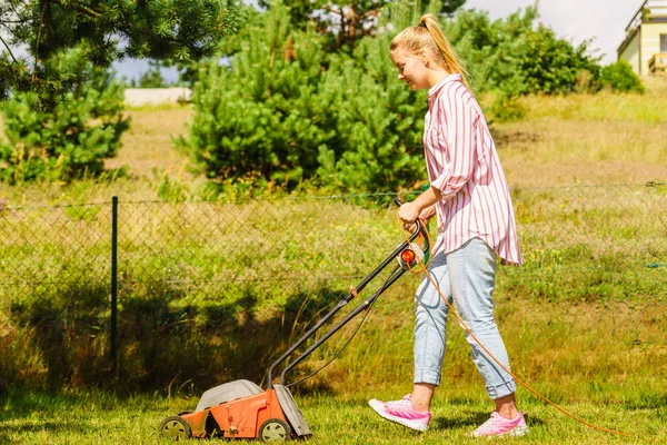Gardening. Female person mowing green lawn with lawnmower in sunny day.