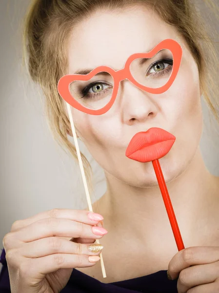 快乐的金发女人拿着嘉年华饰品 戴着假红唇和纸制心形眼镜 玩得很开心 在灰墙背景下 — 图库照片