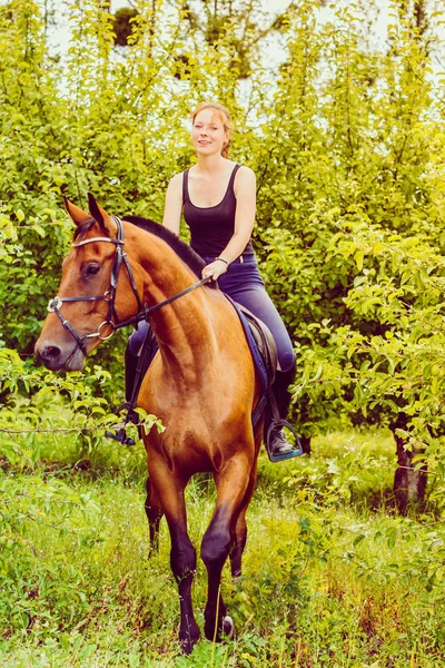 马术的概念 春日的晴天 年轻女子骑着马穿过花园 — 图库照片