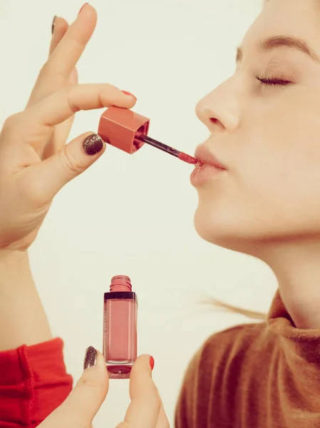 Young adult woman applying lipstick or lip gloss on her lips getting her make up done.