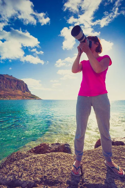 海岸で写真を撮るカメラを持つ女性 背景にはロッキー島のMonemvasia ギリシャ ペロポネソス ラコニア 目的地 — ストック写真