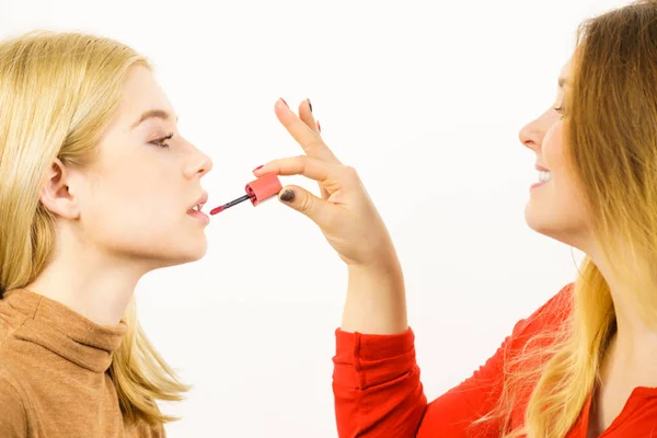 化妆师的朋友在唇上涂抹另一位女性口红或唇彩 两个对面貌感兴趣的朋友 — 图库照片
