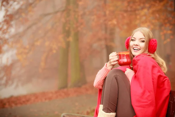 幸福と秋の概念 ベンチで秋の公園でリラックスした若い幸せな女性は温かい飲み物でマグカップを保持熱い飲み物を楽しんでいます オレンジの葉の背景 — ストック写真