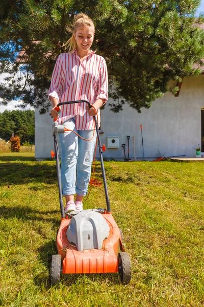 Gardening, taking care of house backyard, agricultural concept. Female person mowing green lawn with lawnmower in sunny day.