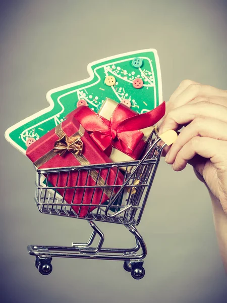 クリスマス 季節の販売 冬のお祝いの概念 女性の手は小さなクリスマスツリーと内側の贈り物とショッピングトロリーカートバスケットを保持 — ストック写真