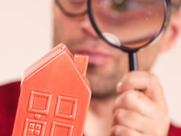 Person examining red model home using a magnifying glass, house inspection and real estate concept