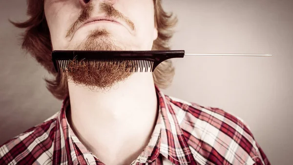 Bearded man having trouble with combing his beard using comb brush. Facial hair concept.