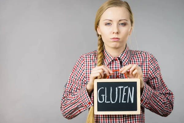 Young woman with braided hair holding small black board with gluten sign. Bakery and bread allergy problem.