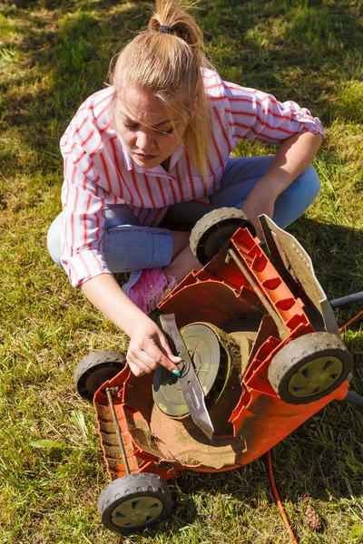 Gardening. Female person gardener mowing green lawn with lawnmower, having problem with broken mower