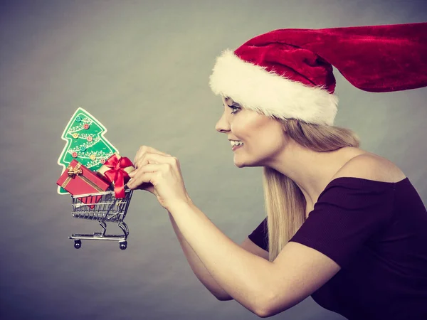 クリスマス 季節的な販売 冬の祭典概念 小さなクリスマス ツリーとギフトの販売のためのランニング中でバスケット ショッピングカート サンタ クロース ヘルパー帽子持株を着て幸せな女 — ストック写真