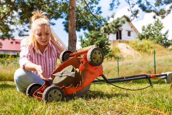 Gardening. Female person gardener mowing green lawn with lawnmower, having problem with broken mower