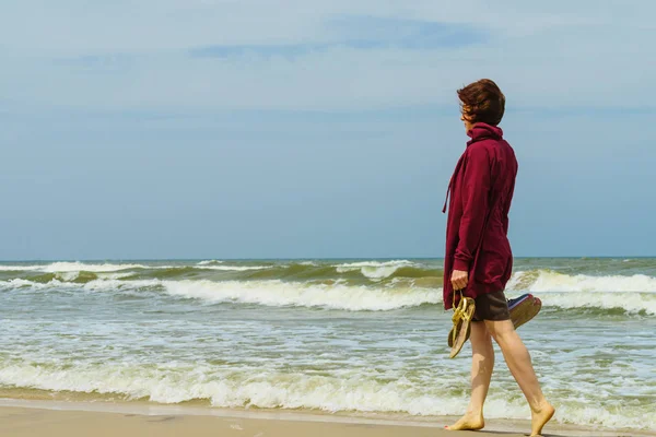 在温暖的秋天里 女人有闲暇时间赤脚在海滩上散步 手里拿着鞋子凉鞋 — 图库照片