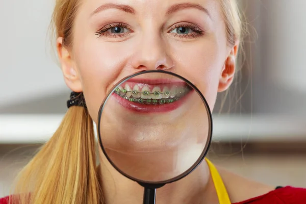 Dentistry and stomatology concept. Happy smiling woman showing her braces on teeth through magnifying glass
