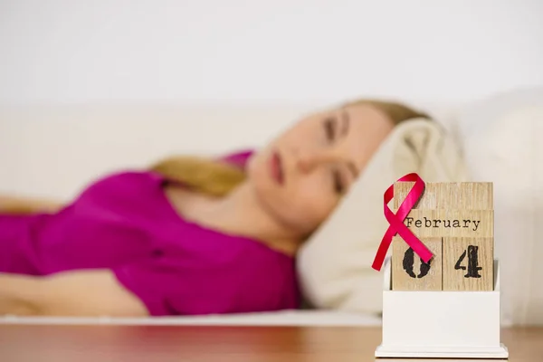 女人躺在床上看日历 今天是2月4日世界乳腺癌日 与粉色的意识带约会 保健和医药概念 — 图库照片