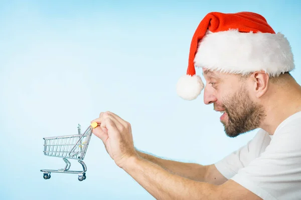 Mann Mit Weihnachtsmann Mütze Und Leerem Einkaufswagen Auf Blauem Grund — Stockfoto