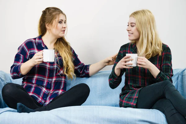 2人の女性の友人一緒にソファでおしゃべりやお茶やコーヒーを飲みながら座って一緒に時間を過ごす — ストック写真