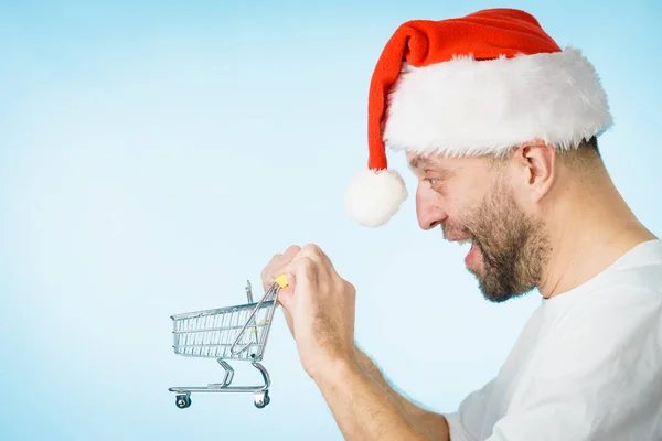 Mann Mit Weihnachtsmann Mütze Und Leerem Einkaufswagen Auf Blauem Grund — Stockfoto