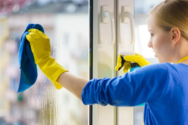 穿着黄色手套的年轻女子在家里用抹布和喷雾清洁剂擦拭窗玻璃 清洗概念 — 图库照片