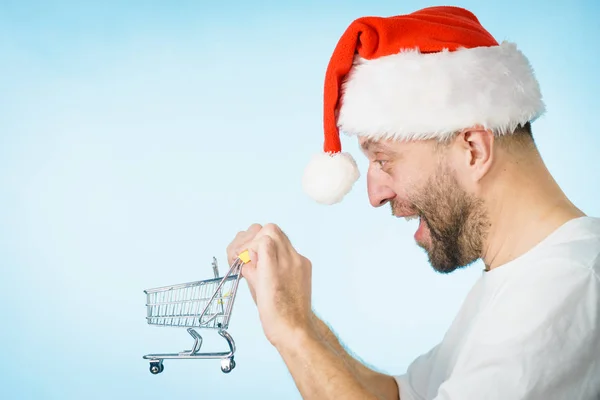 头戴圣诞礼帽的男人拿着空购物篮推车 蓝色的 圣诞节 季节性销售 拳击日的概念 — 图库照片