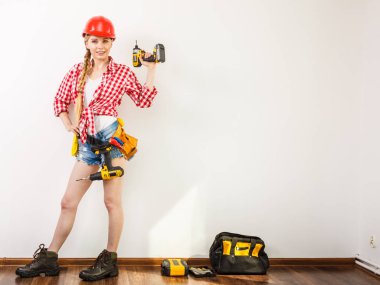 Woman wearing helmet using drill. Girl working at flat remodeling. Building, repair and renovation. clipart