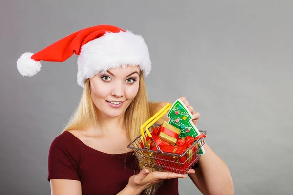 圣诞节 季节性销售 冬季庆祝的概念 快乐的女人头戴圣诞礼帽 手里拿着购物篮车 里面有小圣诞树和礼物 — 图库照片