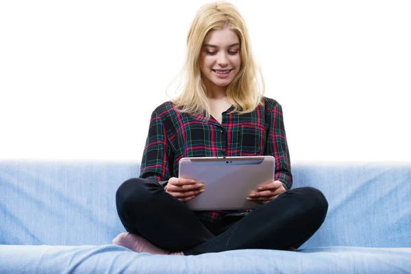 年轻的少女坐在沙发上 一边用平板电脑一边放松地上网 — 图库照片