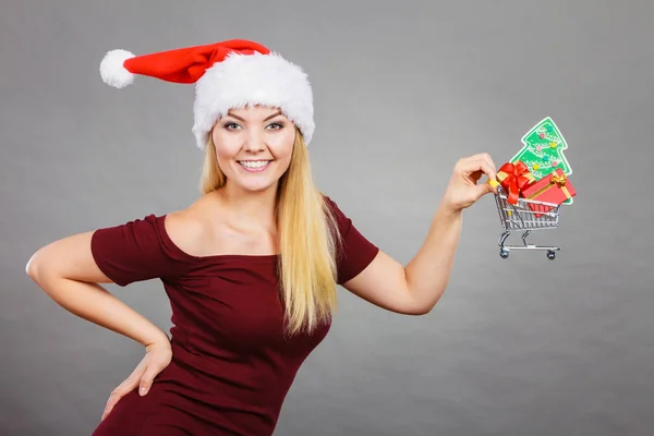 圣诞节 季节性销售 冬季庆祝的概念 快乐的女人头戴圣诞礼帽 手里拿着购物篮车 里面有小圣诞树和礼物 — 图库照片