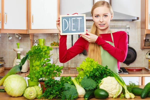 若い女性がキッチンで多くの緑の野菜を持っている食事の看板とボードを提示 — ストック写真