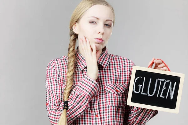 Young woman with braided hair holding small black board with gluten sign. Bakery and bread allergy problem.