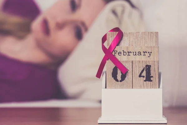 女人躺在床上看日历 今天是2月4日世界乳腺癌日 与粉色的意识带约会 保健和医药概念 — 图库照片