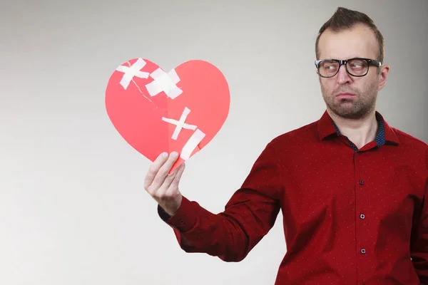 stock image Bad relationships, breaking up, sadness emotions concept. Sad adult man holding broken heart fixed with plaster bandage, on grey