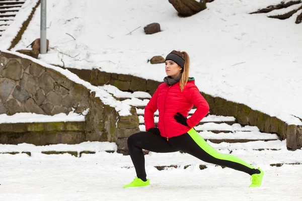 Outdoor sport exercising, sporty outfit ideas. Woman wearing warm sportswear training exercising stretching legs outside during winter.