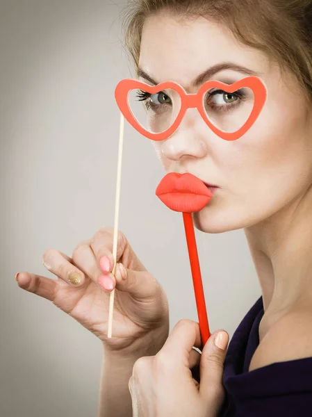 幸せなブロンドの女性は 楽しさを持って 偽の赤い唇や紙の心の形のメガネに固執するカーニバルアクセサリーを保持 灰色の壁の背景に — ストック写真