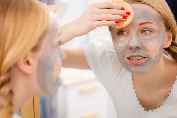 Mulher removendo máscara facial de lama com esponja — Fotografia de Stock