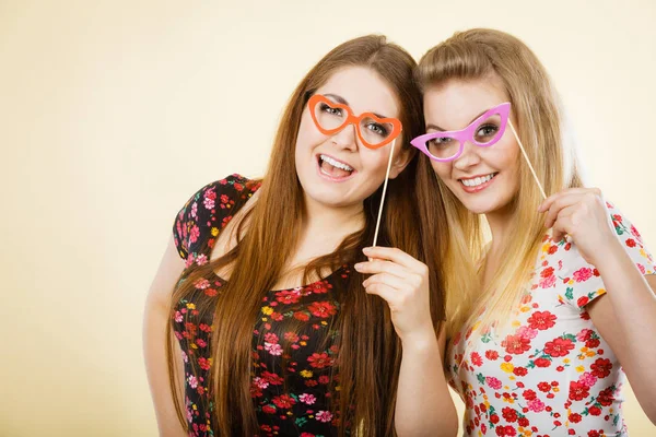 Two happy women holding fake eyeglasses on stick — Stock Photo, Image